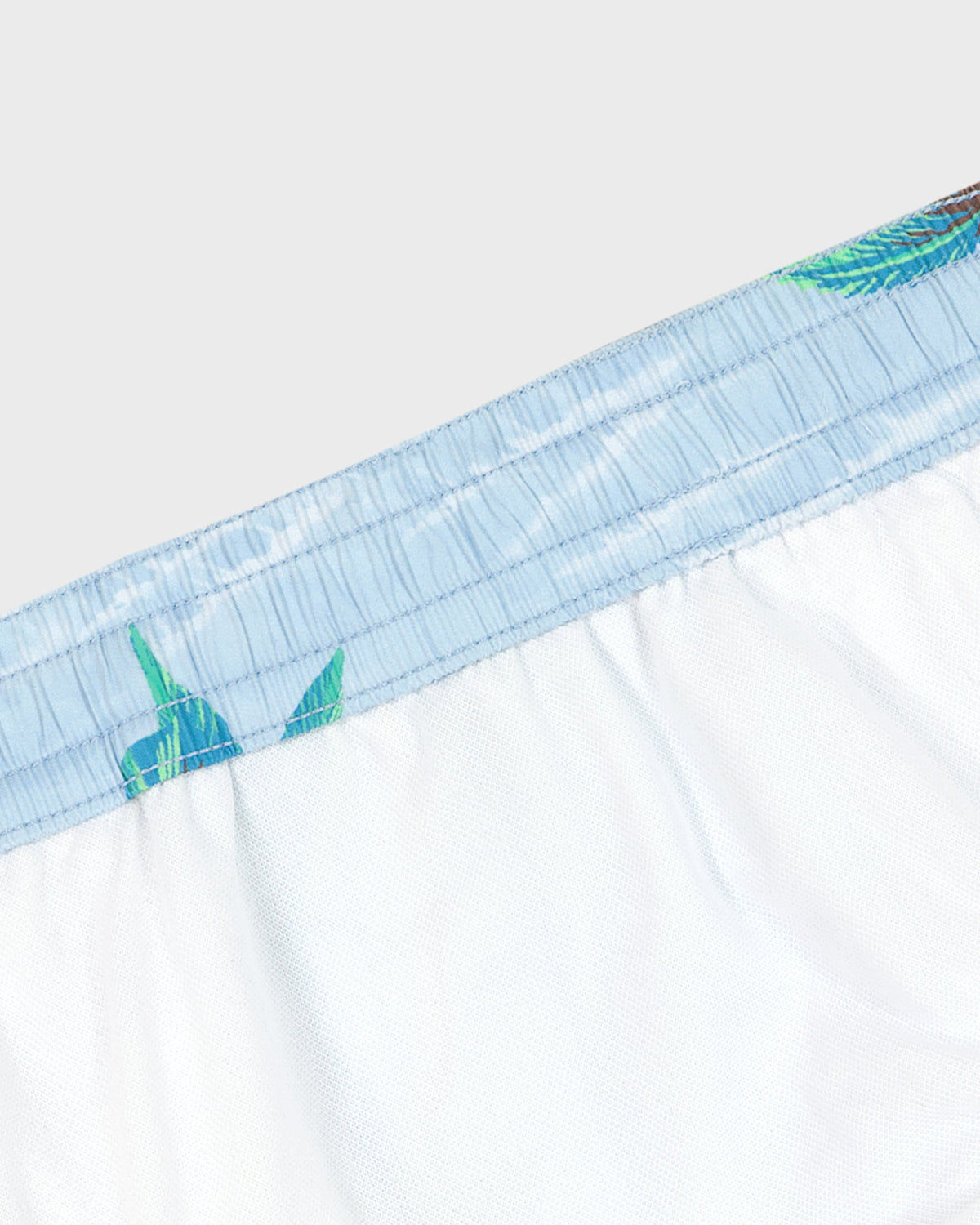 Close-up of white boxer briefs with blue and green trim on a light gray background